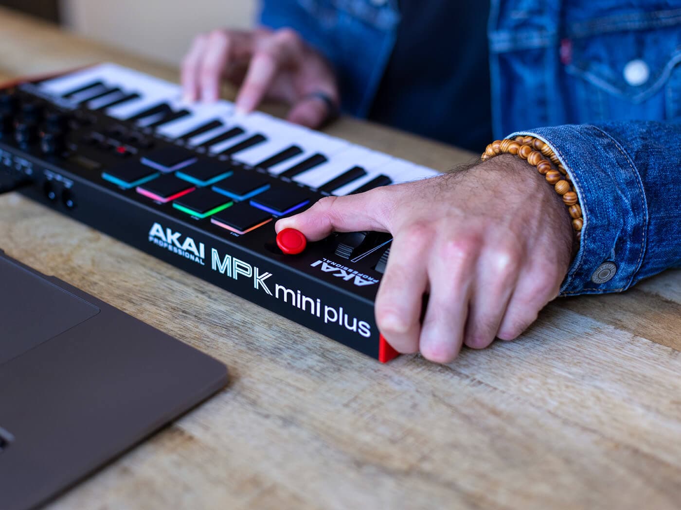 Hands playing an Akai MPK Mini MIDI keyboard next to a laptop