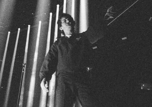 Joe Keery performing as Djo beneath vertical stage lights