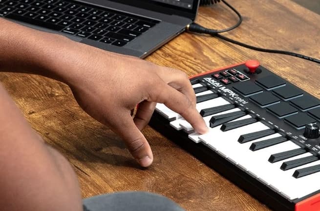 A musician playing an Akai MPK Mini MIDI keyboard next to a laptop