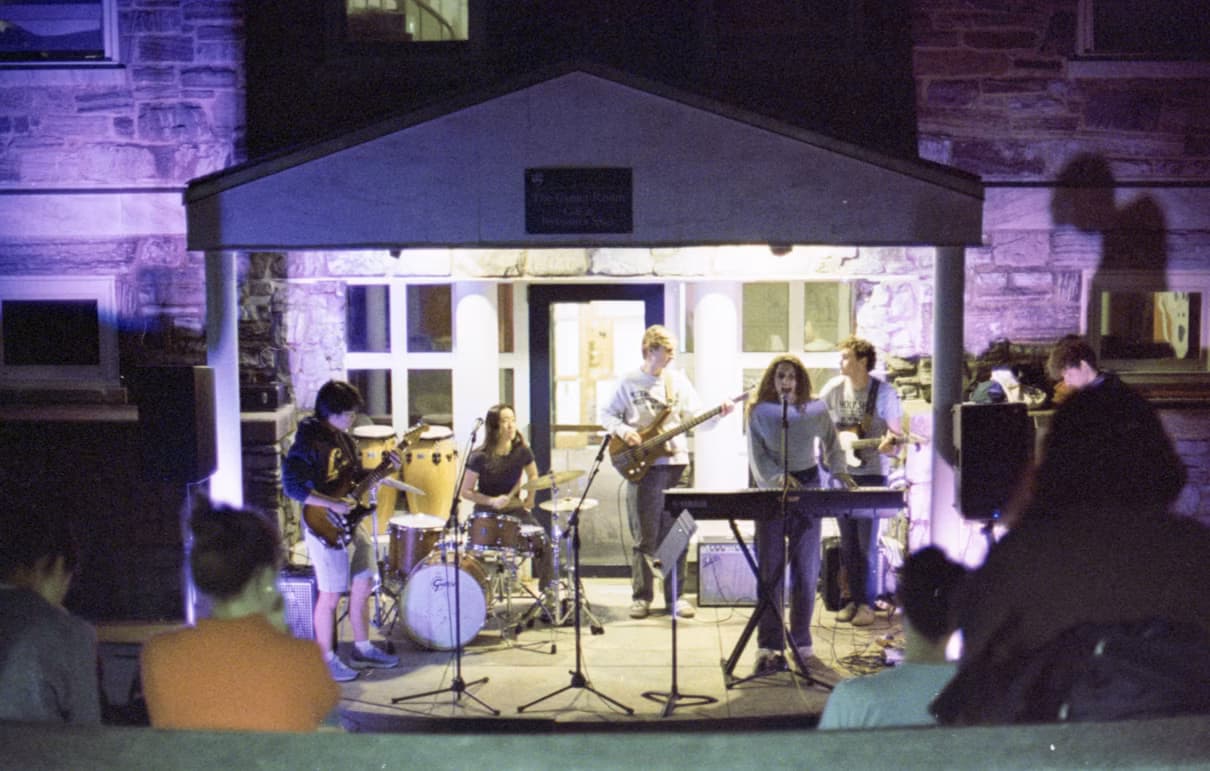 A musician performing guitar at a crowded campus show