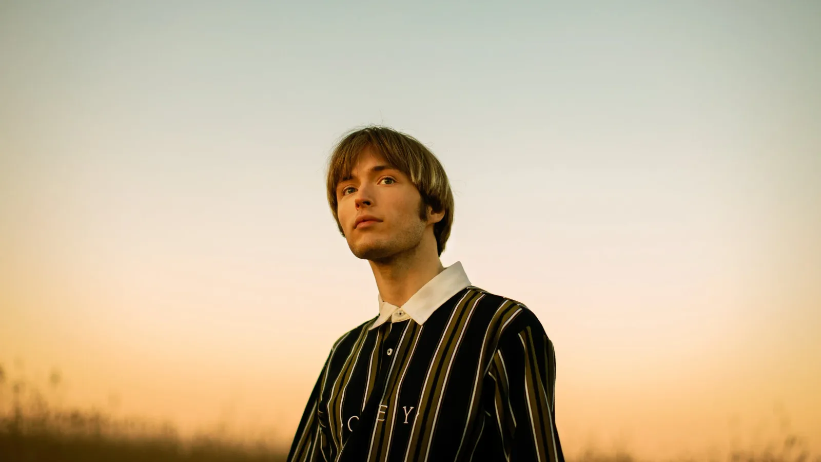 Jakob Ogawa standing outdoors against a warm sunset sky