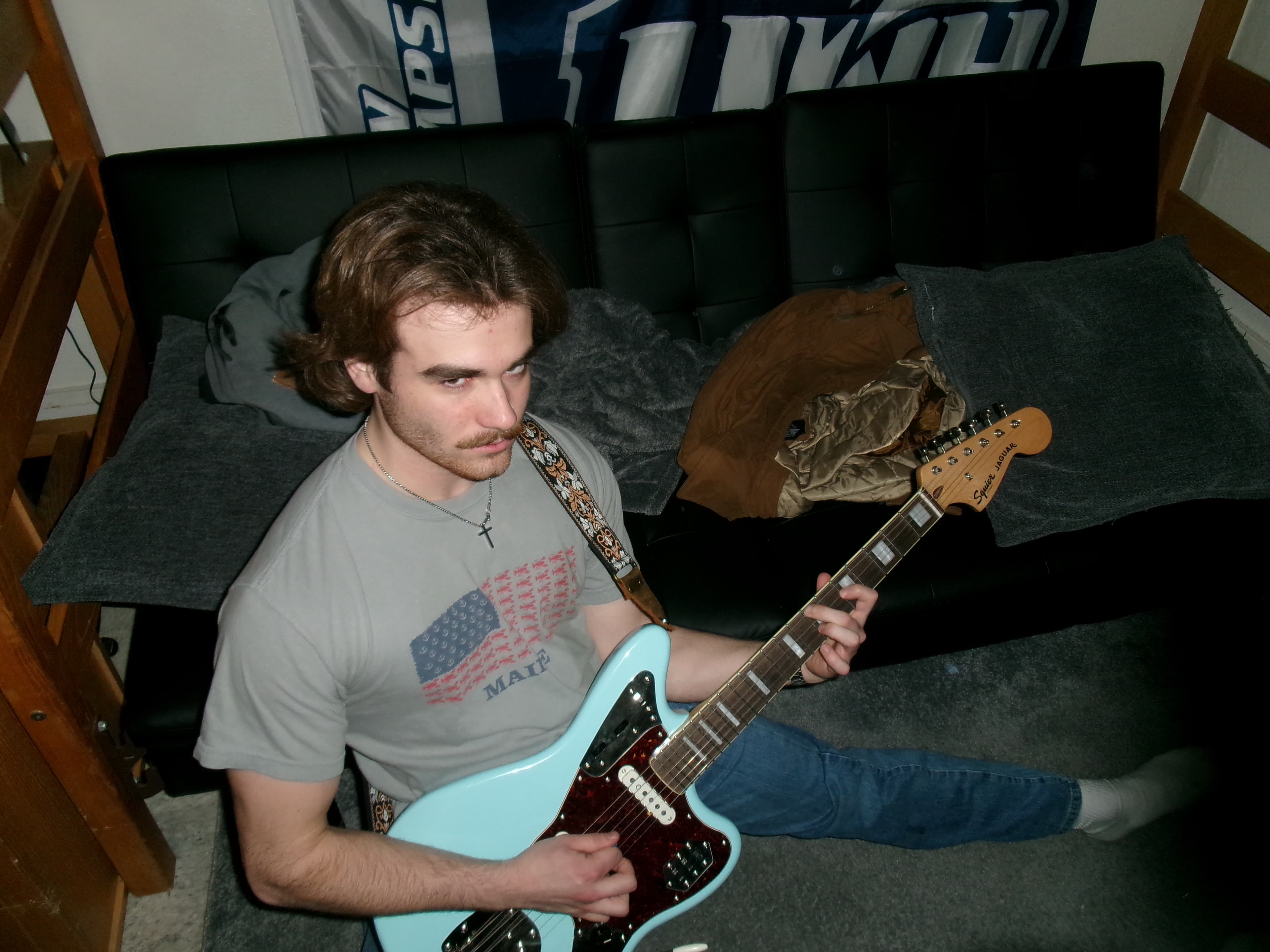 A guitarist sitting with a surf green electric guitar in a bedroom practice space